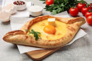 Photo of Tasty khachapuri with cheese, egg, parsley and other products on light grey background, closeup