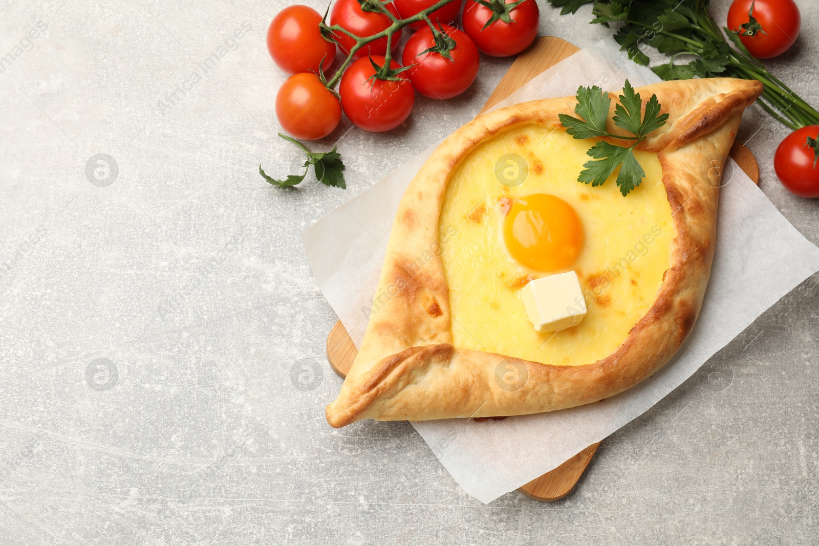 Tasty khachapuri with cheese, egg, parsley and other products on light grey background, flat lay. Space for text Photo of Tasty khachapuri with cheese, egg, parsley and other products on light grey background, flat lay. Space for text