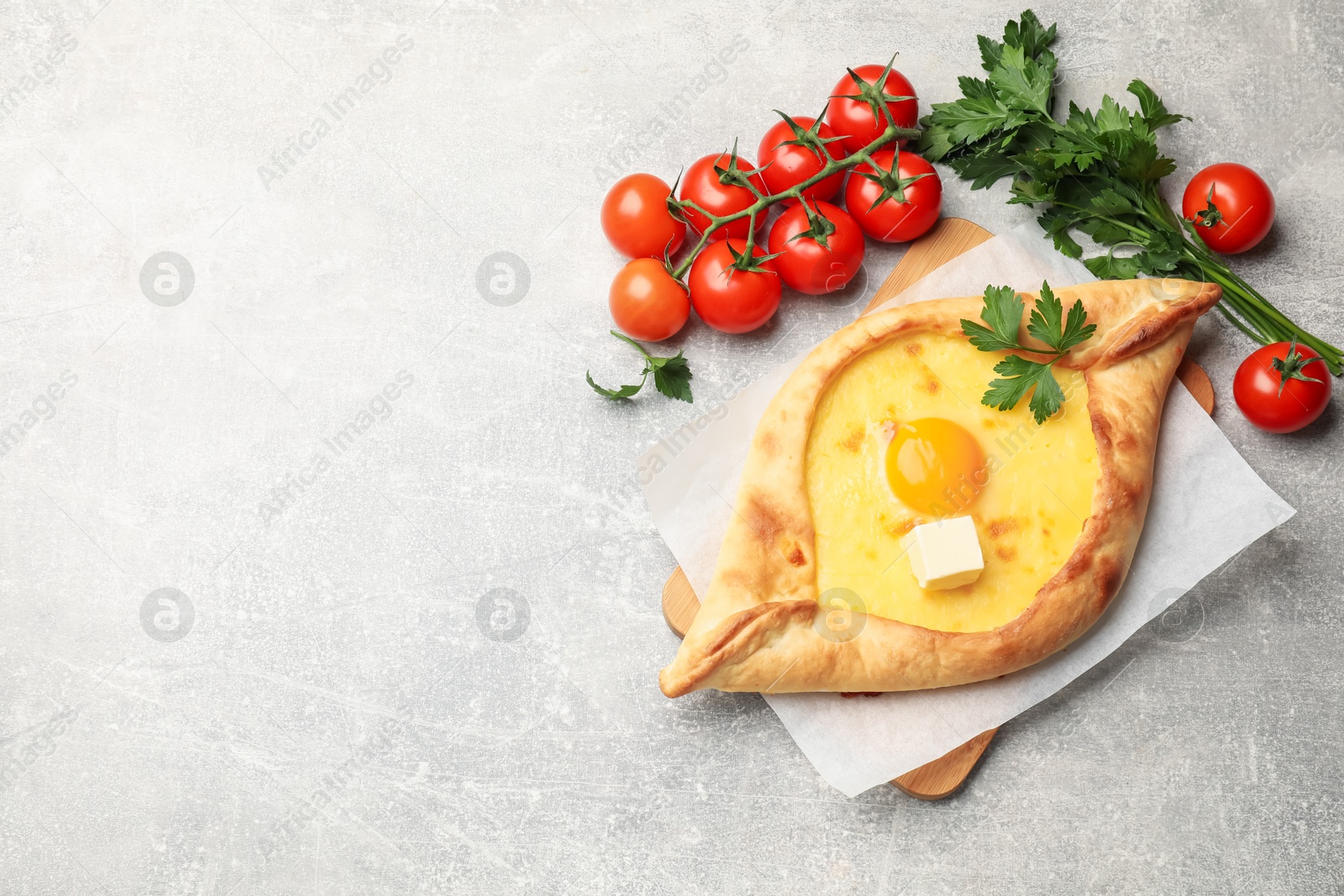 Tasty khachapuri with cheese, egg, parsley and other products on light grey background, flat lay. Space for text Photo of Tasty khachapuri with cheese, egg, parsley and other products on light grey background, flat lay. Space for text