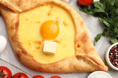 Photo of Tasty khachapuri with cheese, egg and other products on light grey background, flat lay