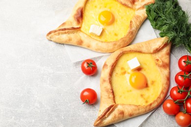 Photo of Tasty khachapuri with cheese, egg and other products on light grey background, flat lay. Space for text