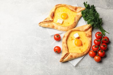 Photo of Tasty khachapuri with cheese, egg and other products on light grey background, flat lay. Space for text