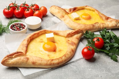 Photo of Tasty khachapuri with cheese, egg and other products on light grey background, closeup