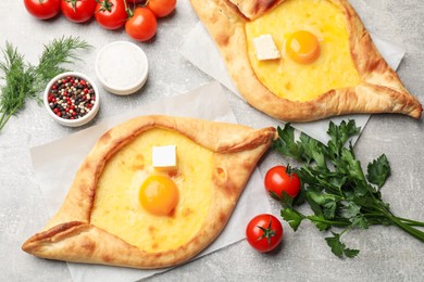Photo of Tasty khachapuri with cheese, egg and other products on light grey background, flat lay