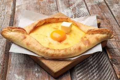 Photo of Tasty khachapuri with cheese and egg on wooden table, closeup