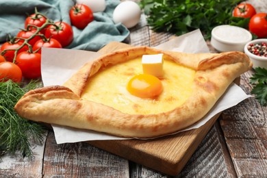 Photo of Tasty khachapuri with cheese, egg and other products on wooden table, closeup