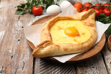 Photo of Tasty khachapuri with cheese, egg and other products on wooden table, closeup