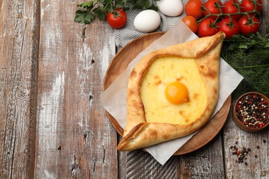 Photo of Tasty khachapuri with cheese, egg and other products on wooden table, flat lay. Space for text