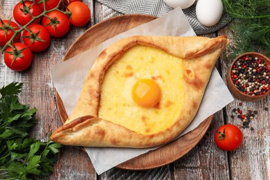 Photo of Tasty khachapuri with cheese, egg and other products on wooden table, flat lay