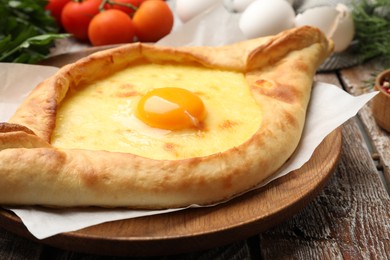 Photo of Tasty khachapuri with cheese, egg and other products on wooden table, closeup