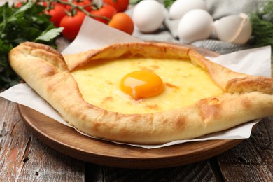 Photo of Tasty khachapuri with cheese, egg and other products on wooden table, closeup