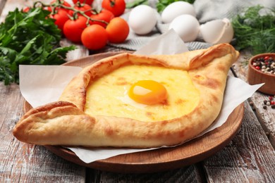 Photo of Tasty khachapuri with cheese, egg and other products on wooden table, closeup