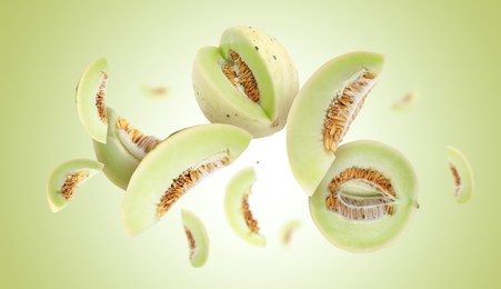 Image of Cut fresh ripe melons swirling in air against light green gradient background