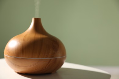 Photo of One stylish aroma lamp on white table against green wall, closeup. Space for text