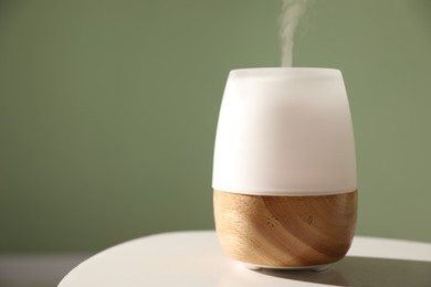 Photo of One stylish aroma lamp on white table against green wall, closeup. Space for text