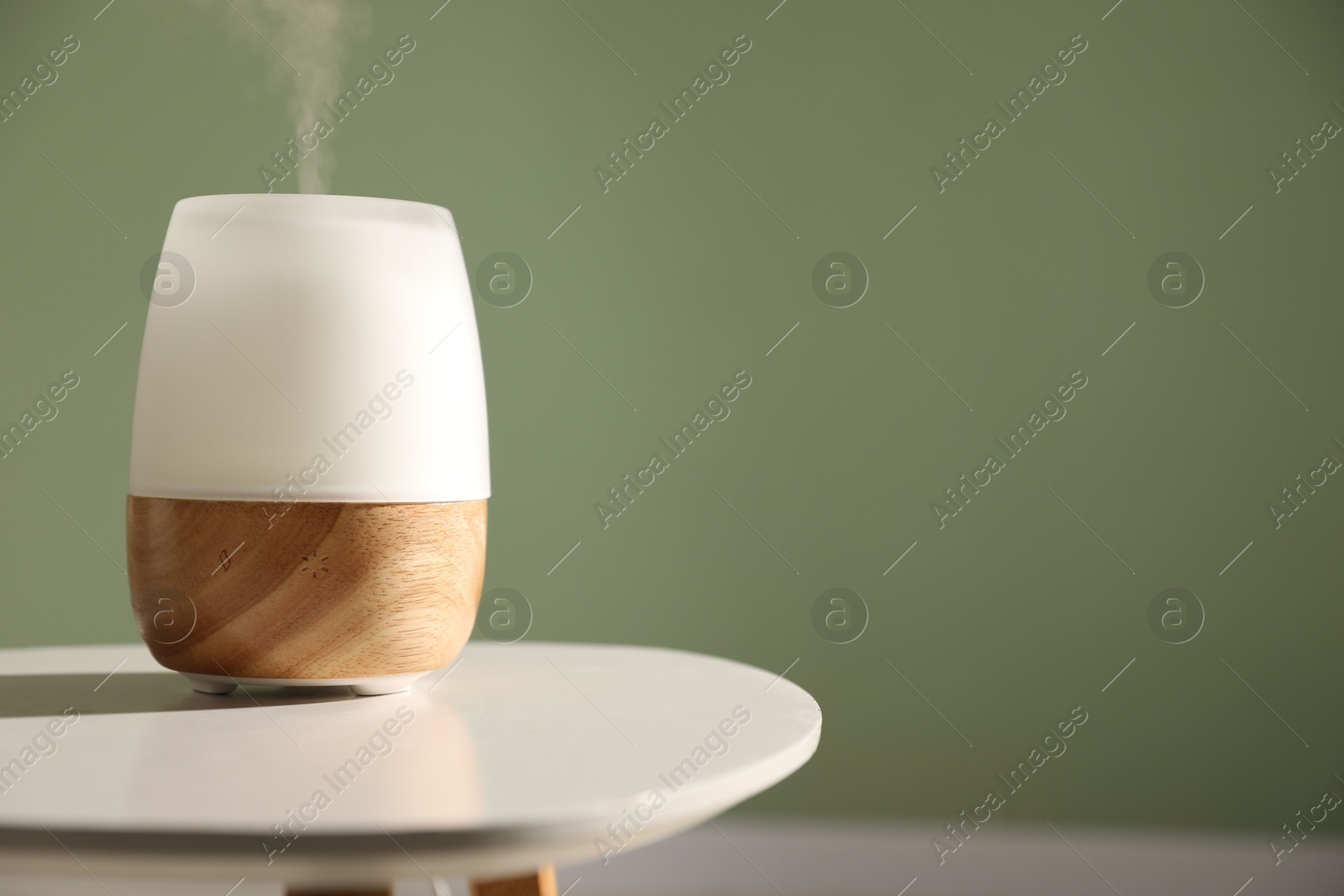 Photo of One stylish aroma lamp on white table against green wall, closeup. Space for text
