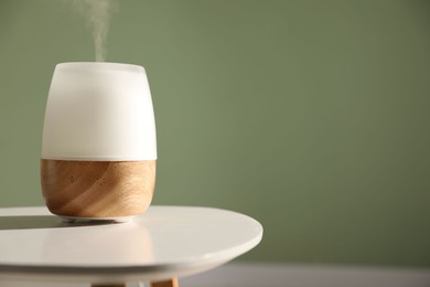 Photo of One stylish aroma lamp on white table against green wall, closeup. Space for text