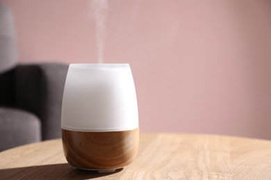Photo of One stylish aroma lamp on wooden table against pink wall, closeup. Space for text