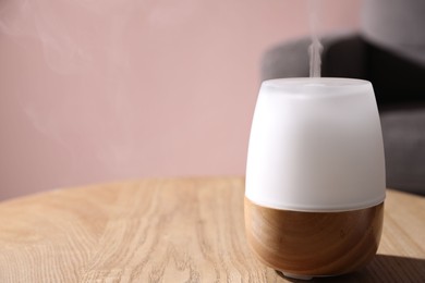 Photo of One stylish aroma lamp on wooden table against pink wall, closeup. Space for text