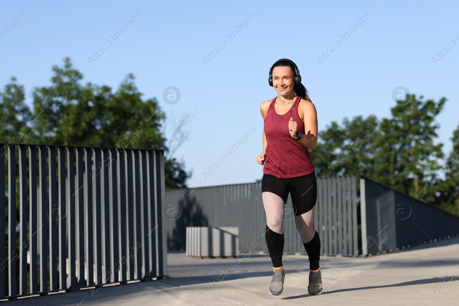 Athletic young woman with headphones in sportswear running outdoors, space for text Photo of Athletic young woman with headphones in sportswear running outdoors, space for text