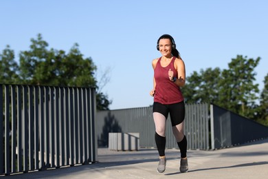 Photo of Athletic young woman with headphones in sportswear running outdoors, space for text