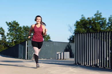 Photo of Athletic young woman with headphones in sportswear running outdoors, space for text