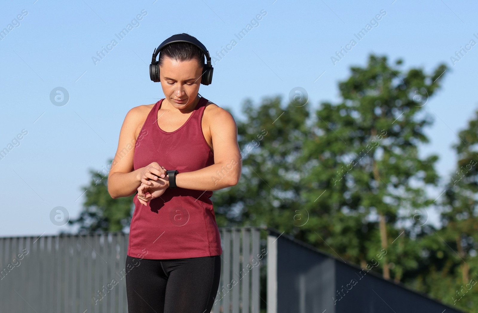Athletic young woman with headphones checking fitness tracker before running outdoors, space for text Photo of Athletic young woman with headphones checking fitness tracker before running outdoors, space for text