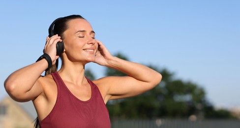 Photo of Athletic young woman with headphones in sportswear before running outdoors, space for text