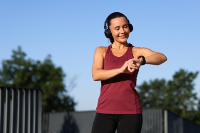 Photo of Athletic young woman with headphones checking fitness tracker before running outdoors, space for text