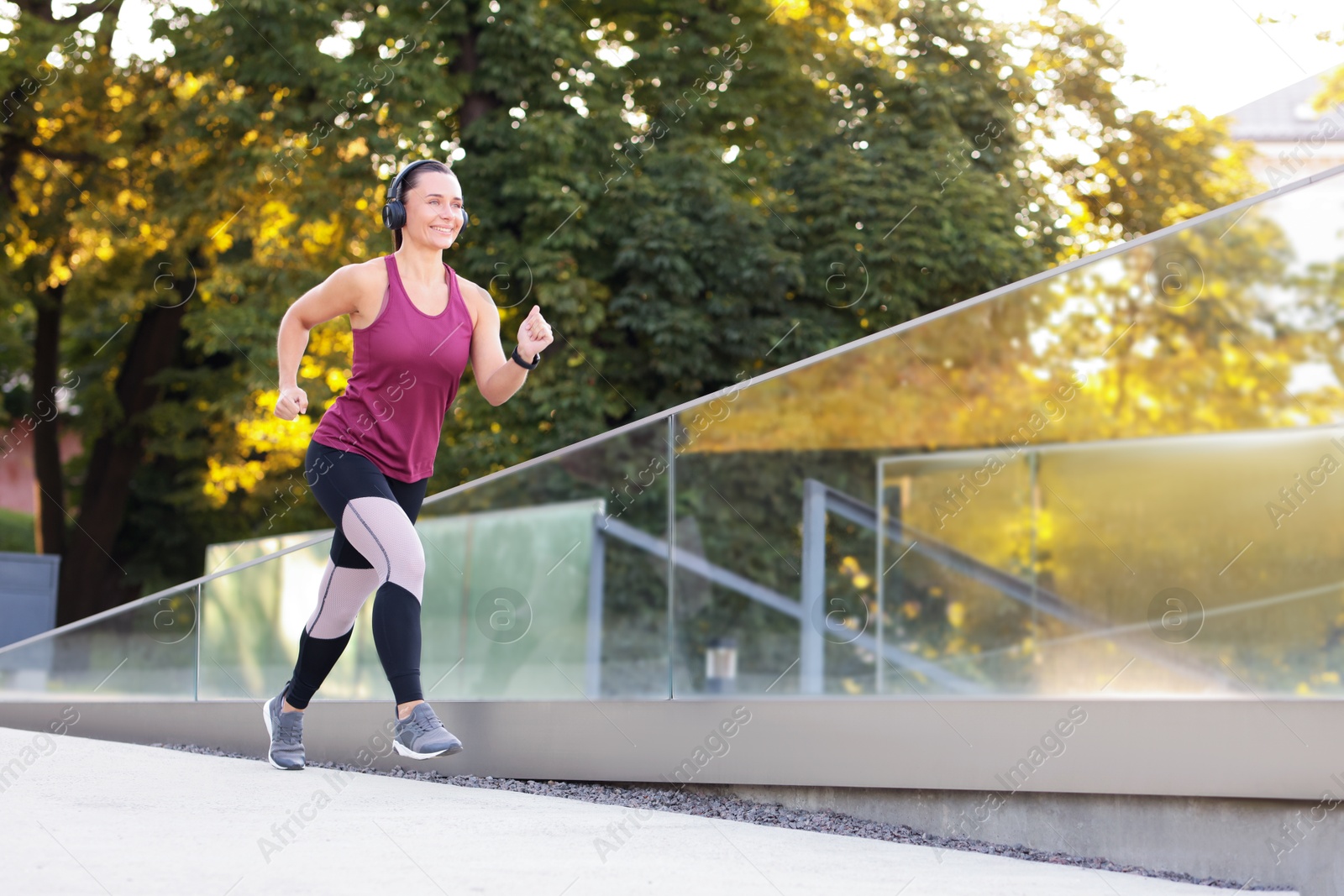 Athletic young woman with headphones in sportswear running outdoors, space for text Photo of Athletic young woman with headphones in sportswear running outdoors, space for text