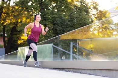 Photo of Athletic young woman with headphones in sportswear running outdoors, space for text