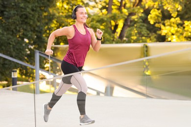 Photo of Athletic young woman with headphones in sportswear running outdoors, space for text