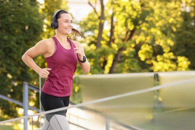 Photo of Athletic young woman with headphones in sportswear running outdoors, space for text