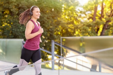 Photo of Athletic young woman with headphones in sportswear running outdoors, space for text