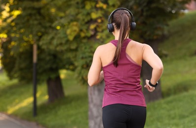 Photo of Athletic young woman with headphones in sportswear running outdoors, back view. Space for text