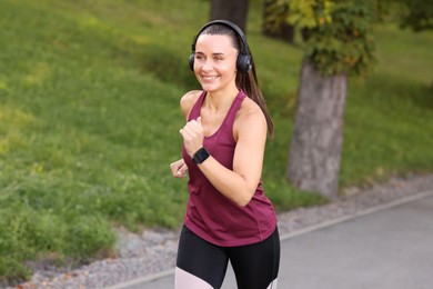 Photo of Athletic young woman with headphones in sportswear running outdoors