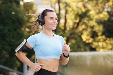 Photo of Athletic young woman with headphones running outdoors, space for text