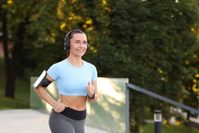 Photo of Athletic young woman with headphones running outdoors, space for text