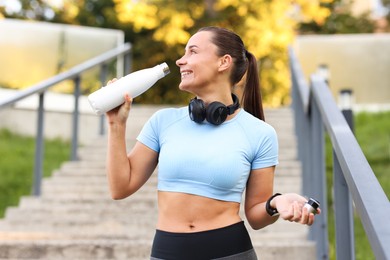 Photo of Athletic young woman with headphones drinking water before running outdoors