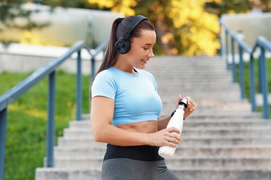 Photo of Athletic young woman with headphones in sportswear before running outdoors