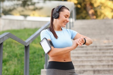 Photo of Athletic young woman with headphones checking fitness tracker before running outdoors