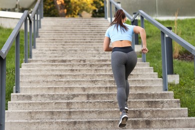Photo of Woman in sportswear running up on stairs outdoors, low angle view. Space for text