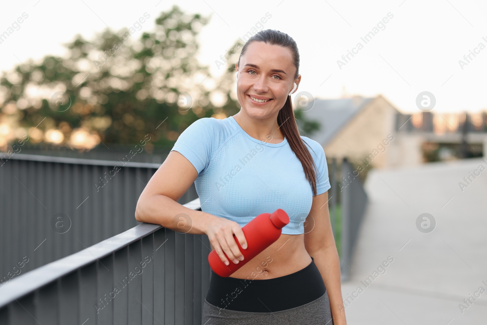 Young woman with earphones and bottle of water before running outdoors Photo of Young woman with earphones and bottle of water before running outdoors