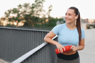 Photo of Young woman with earphones and bottle of water before running outdoors, space for text