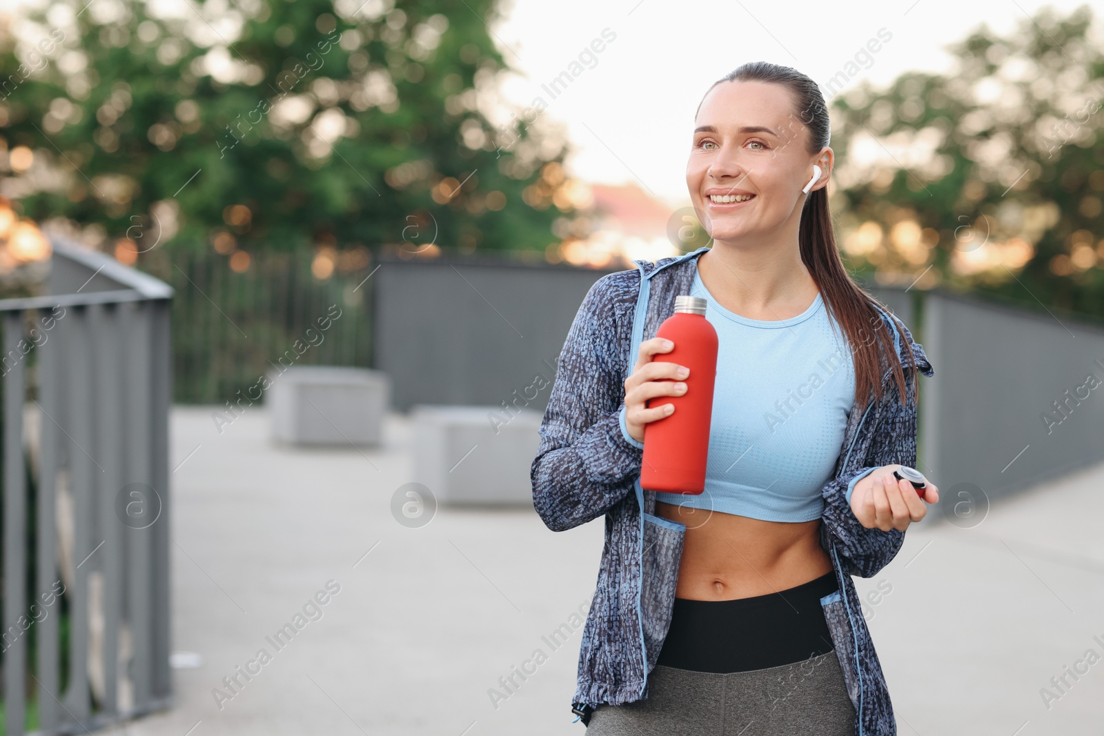 Young woman with earphones and bottle of water before running outdoors, space for text Photo of Young woman with earphones and bottle of water before running outdoors, space for text