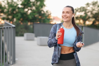 Photo of Young woman with earphones and bottle of water before running outdoors, space for text