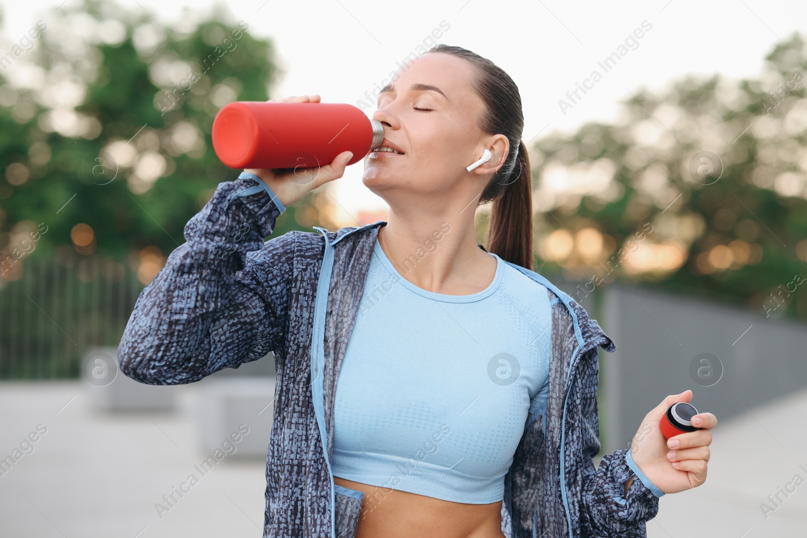 Young woman with earphones drinking water before running outdoors Photo of Young woman with earphones drinking water before running outdoors