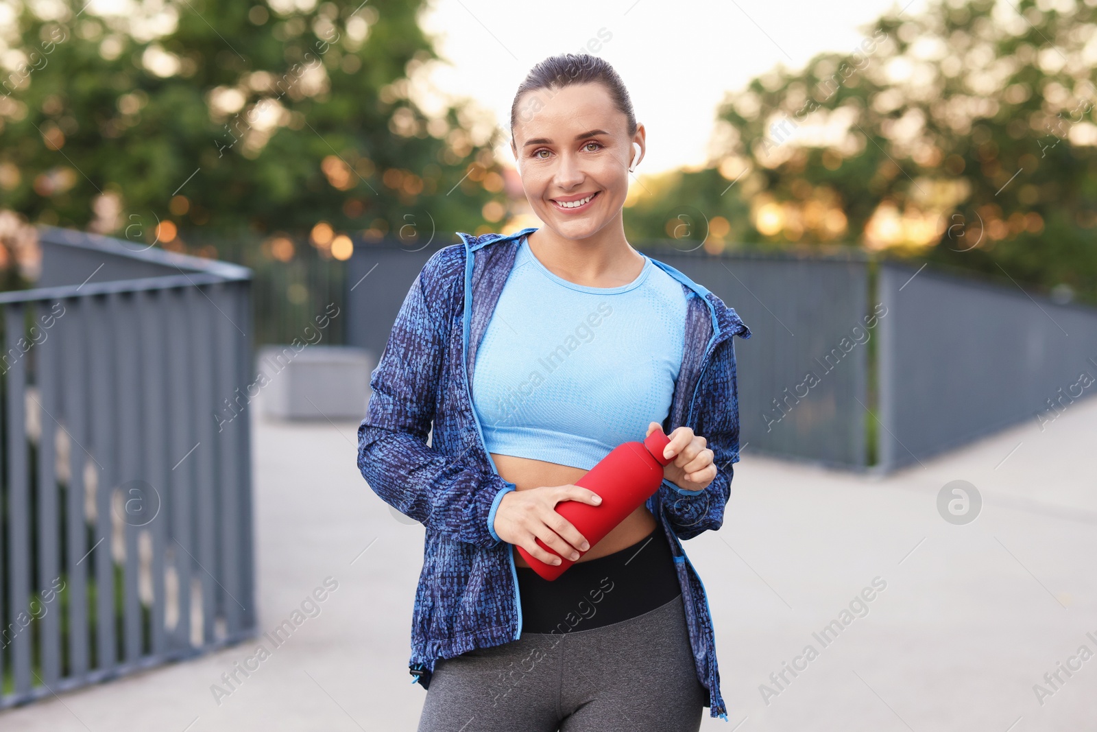 Young woman with earphones and bottle of water before running outdoors Photo of Young woman with earphones and bottle of water before running outdoors