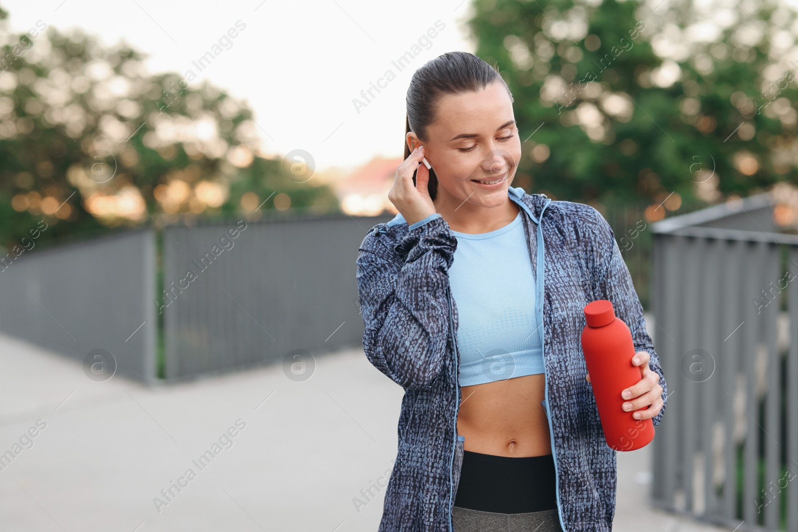 Young woman with earphones and bottle of water before running outdoors, space for text Photo of Young woman with earphones and bottle of water before running outdoors, space for text