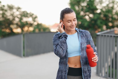 Photo of Young woman with earphones and bottle of water before running outdoors, space for text